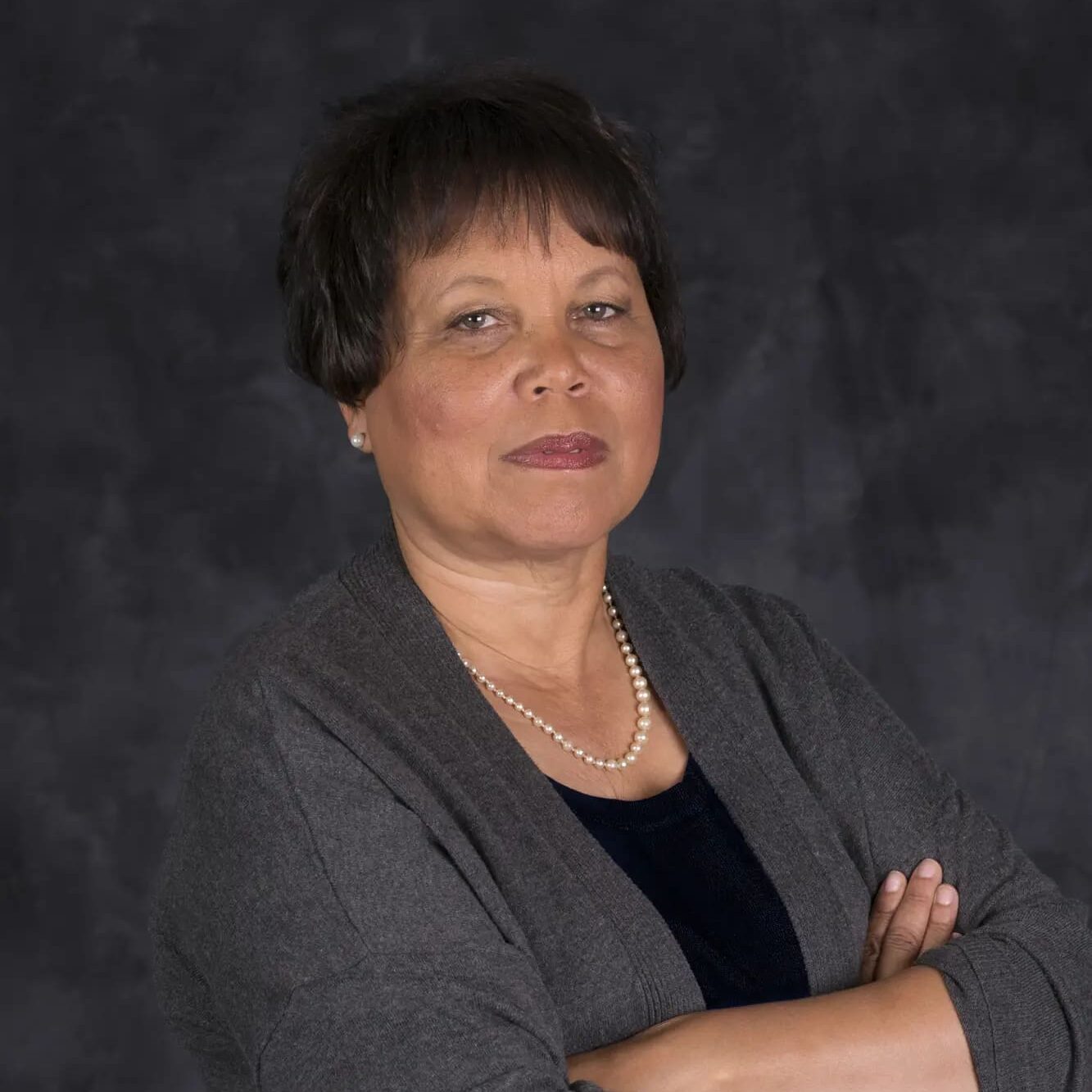 A woman with her arms crossed in front of a black background.